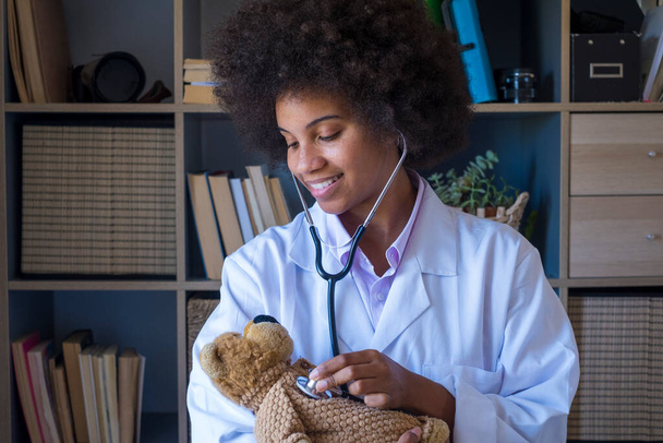 Happy Afro-Amerikaanse vrouwelijke arts in medisch uniform houden gevuld speelgoed met zorg liefde voor kleine patiënt, glimlachende vrouw arts kinderarts controleren hartslag adem van teddybeer in het ziekenhuis of kliniek  - Foto, afbeelding