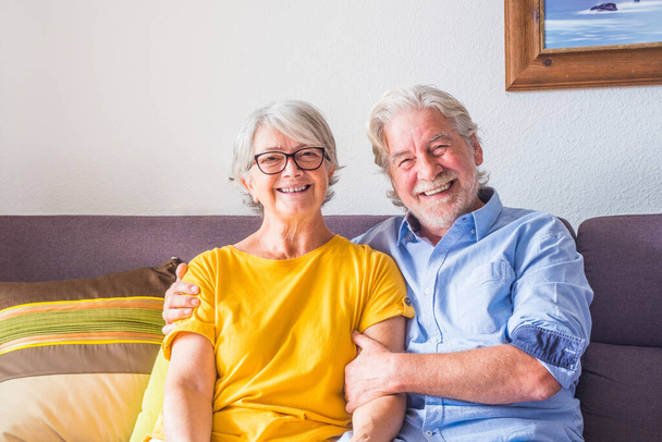 pareja de dos personas mayores felices o personas maduras sonriendo y mirando a la cámara sentado en el sofá en casa - retrato de los pensionistas sentados en el sofá en el interior   - Foto, Imagen