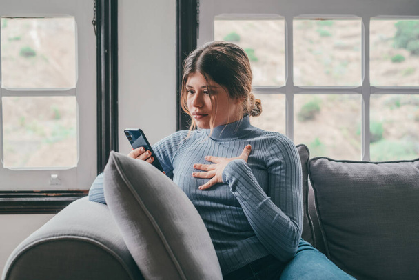 Portrait of impressed pretty female person staring phone bad fake news isolated on sofa at home. Young woman looking and reacting to something.  - Photo, Image