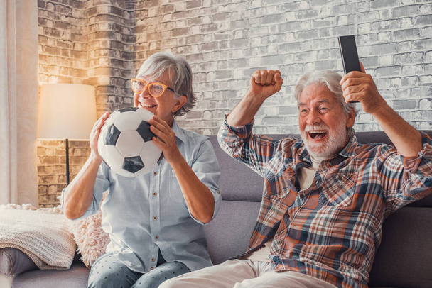 Feliz pareja de personas mayores o aficionados al fútbol viendo el fútbol en la televisión y celebrando la victoria en casa. Concepto de familia, deporte y entretenimiento.  - Foto, Imagen