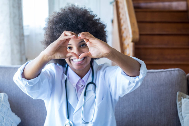 女性医師は手で心臓の形のジェスチャーを行う。黒の女性医師の笑顔彼女の手を使用して愛のシンボルを作る。患者への愛と支援を表現する医療従事者 - 写真・画像