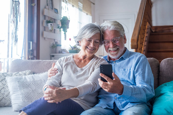 Couple of two old and mature people at home using tablet together in sofa. Senior use laptop having fun and enjoying looking at it. Leisure and free time concept - Photo, Image