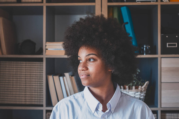 Atrakcyjny ciemnoskóry młoda kobieta z kręconą fryzurą Afro patrząc przez okno. Przemyślana afrykańska amerykańska bizneswoman odwracająca wzrok od biura. Kobieta marzy o przyszłości.  - Zdjęcie, obraz