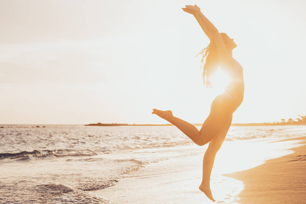 Una giovane donna felice e sana che salta sulla sabbia della spiaggia divertendosi e godendosi l'estate all'aria aperta. Bella ragazza attraente giocare.  - Foto, immagini