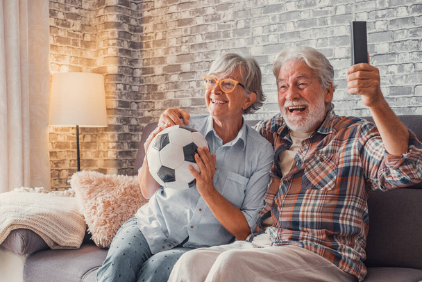 Ευτυχισμένο ζευγάρι ηλικιωμένων ή οπαδών ποδοσφαίρου βλέποντας ποδόσφαιρο στην τηλεόραση και γιορτάζοντας τη νίκη στο σπίτι. Οικογενειακή έννοια, έννοια αθλητισμού και ψυχαγωγίας.  - Φωτογραφία, εικόνα