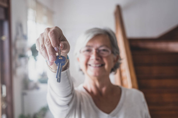 Счастливая пожилая женщина-покупатель держит ключ от квартиры в новом доме в руках фотоаппарата, пожилая женщина-пенсионерка, владеющая недвижимостью, совершает сделку купли-продажи недвижимости, крупным планом  - Фото, изображение