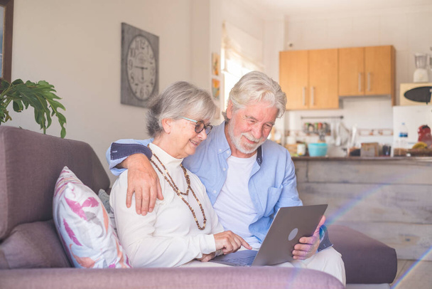 Paar von zwei alten und erwachsenen Menschen zu Hause mit Tablet zusammen auf dem Sofa. Senioren nutzen Laptop mit Spaß und Freude am Betrachten. Freizeit- und Freizeitkonzept  - Foto, Bild
