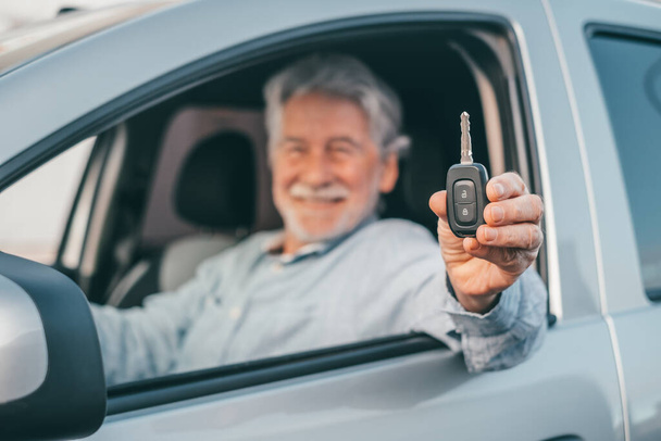 Портрет щасливого старого, який показує ключі від машини до камери. Задоволений клієнт насолоджується своєю новою машиною
. - Фото, зображення