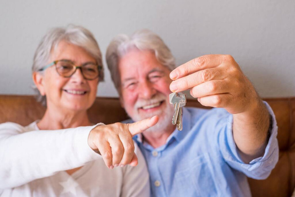 Крупный план пожилой пары, показывающей ключи от дома. Пожилая пара держит ключи для инвестиций в концепцию недвижимости. Удовлетворенная пожилая пара с ключами от нового дома   - Фото, изображение