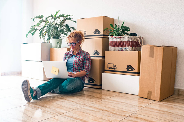One young woman and happy people after buy a new house or apartment together to live together - person on the ground using laptop with boxes and packs on her back    - Photo, Image