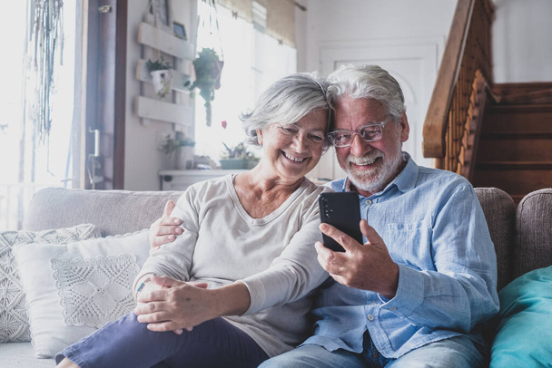 Улыбающаяся взрослая семейная пара постарше проводит мобильный видеозвонок с друзьями, наслаждаясь дистанционным общением со взрослыми детьми, используя приложения для смартфонов дома.  - Фото, изображение