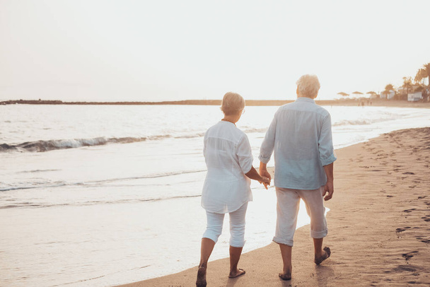 Para starych, dojrzałych ludzi spacerujących razem po piasku i bawiących się na piasku plaży cieszących się chwilą i żyjących nią. Dwóch uroczych seniorów w miłości dobrze się bawiąc. - Zdjęcie, obraz
