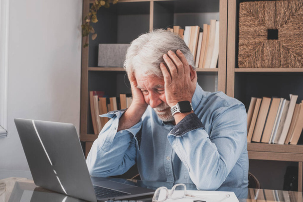 Unhappy frustrated old businessman holding head in hands feeling depressed of having financial trouble. Senior man working at home office using laptop, desperately stressed because of workload - Photo, Image