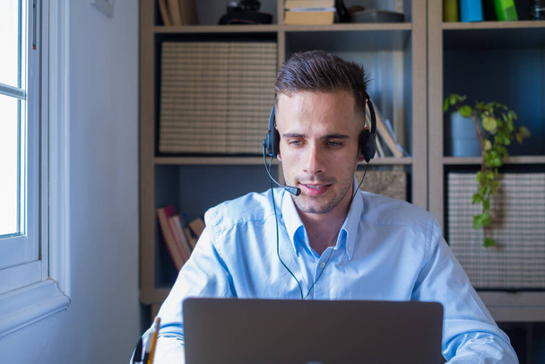Atrakcyjny biały mężczyzna siedzieć w domu biuro pokój noszenie słuchawki wziąć udział w edukacyjnym webinar using laptop. Impreza wideo rozmowy z klientami lub osobisty czat z przyjacielem zdalnie koncepcji  - Zdjęcie, obraz