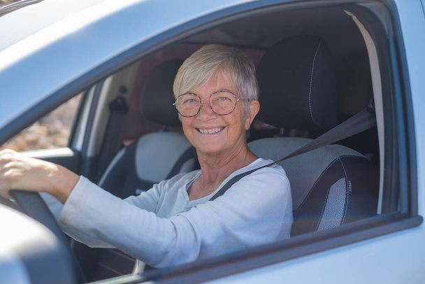Happy owner. Handsome mature woman sitting relaxed in his newly bought car looking out the window smiling joyfully. One old senior driving and having fun.  - Foto, Imagem