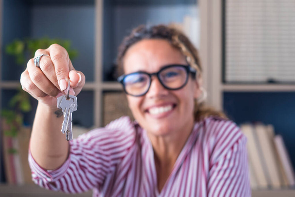 Happy woman showing keys of her new house or office. Portrait of smiling businesswoman holding key to her new apartment. Female tenant or renter moving or relocating with keys in her hand  - Valokuva, kuva