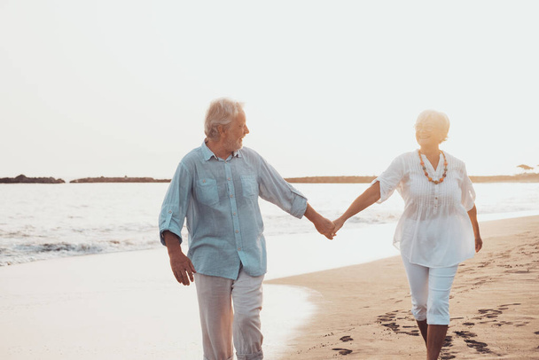 Para starych, dojrzałych ludzi spacerujących razem po piasku i bawiących się na piasku plaży cieszących się chwilą i żyjących nią. Dwoje uroczych seniorów zakochanych w zabawie. boso chodzacy po wodzie - Zdjęcie, obraz