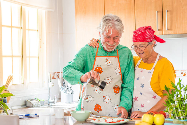 couple de deux aînés heureux de s'amuser et de cuisiner ensemble dans la cuisine de leur maison - préparer des aliments sains avec des tomates   - Photo, image