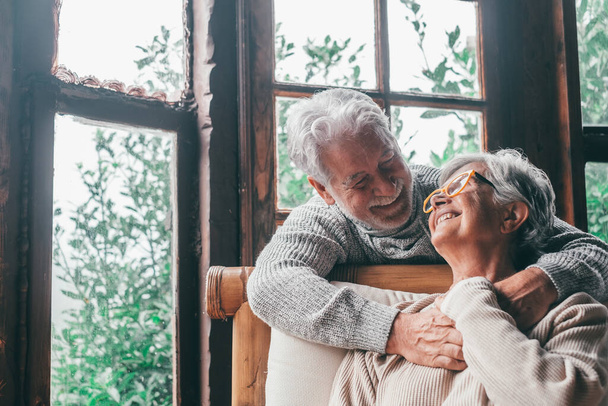 Porträt von zwei glücklichen und gesunden Senioren, die einander lächelnd anschauen. Nahaufnahme von reifen Großeltern genießen und Spaß zusammen zu Hause drinnen.   - Foto, Bild