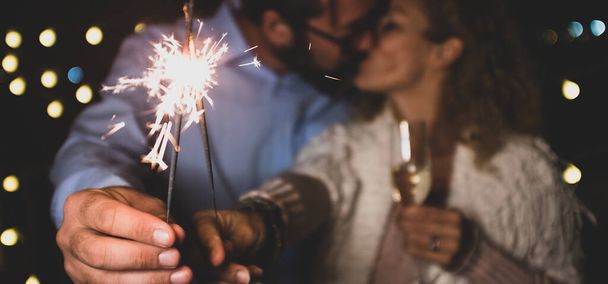 χαριτωμένο ζευγάρι των δύο ενηλίκων στην αγάπη δίνοντας μια απώλεια μαζί το νέο έτος νύχτα παίζοντας με sparklers στο χέρι τους κοντά από την κάμερα φιλιούνται μεταξύ τους  - Φωτογραφία, εικόνα