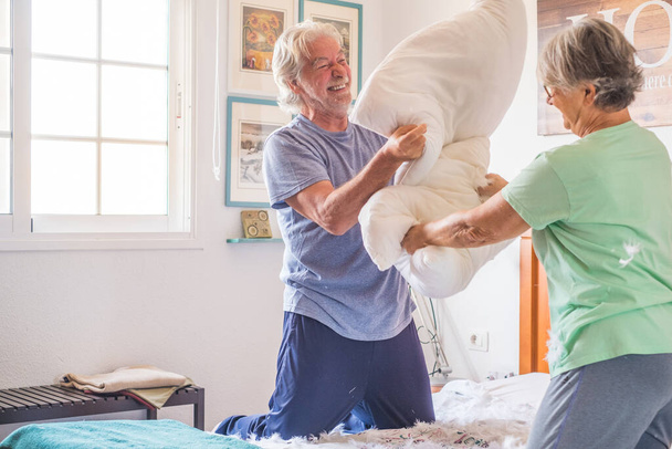 coppia di due anziani felici divertirsi giocando insieme sul letto a casa a combattere con cuscini godendo - cuscini guerra al chiuso al mattino  - Foto, immagini