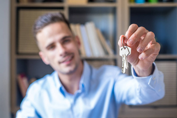 Focus on bunch of keys from house flat apartment in hand of smiling male. Blurred portrait of confident man professional realtor offering new dwelling real estate unit to potential buyer. Close up  - Photo, Image