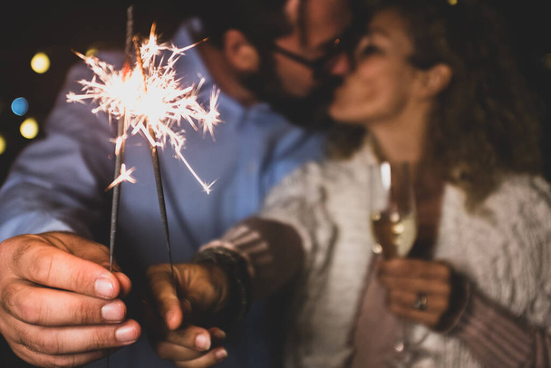 cute couple of two adults in love giving a loss together the new year night playing with sparklers in their hand near of the camera kissing each others  - Foto, Bild