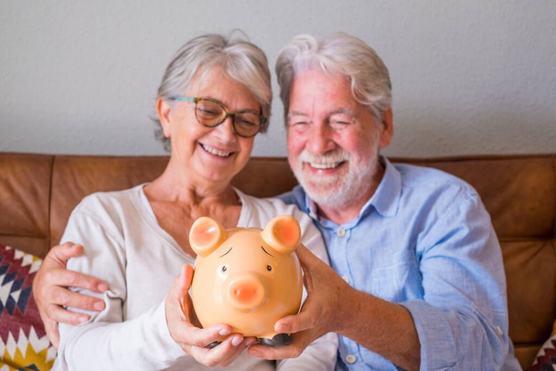Großaufnahme eines älteren Ehepaares, das Sparschwein zeigt, um Geld zu sparen. Älteres Ehepaar hält Sparschwein für Investition und Zukunftskonzept. Glückliches Rentnerpaar hält Sparschwein zu Hause zusammen   - Foto, Bild