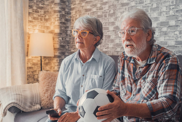 Onnellinen pari eläkeläisiä tai jalkapallofaneja katsomassa jalkapalloa televisiosta ja juhlimassa voittoa kotona. Perheen, urheilun ja viihteen käsite. - Valokuva, kuva
