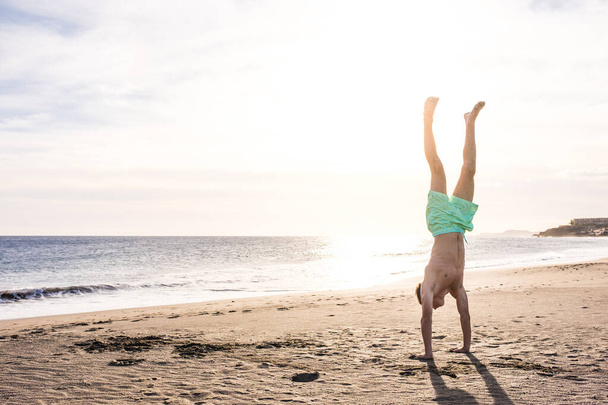 homme faisant un stand de tête sur le sable de la plage au coucher du soleil seul mode de vie sain et agréable en été   - Photo, image
