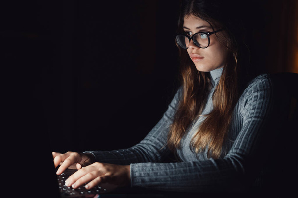 自宅で深夜に働いているコンピューターを使って美しく若い女性がいます。白人ティーン身に着けていますアイグラス研究のためにテスト.  - 写真・画像