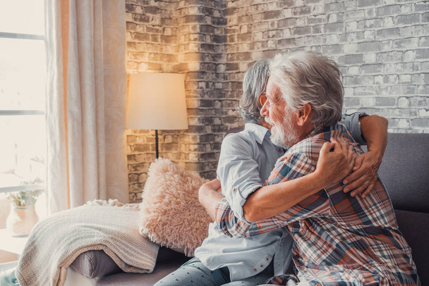Een paar oude senioren knuffelen elkaar en zorgen thuis op de bank voor elkaar. Volwassen mensen in de liefde genieten van het leven. - Foto, afbeelding