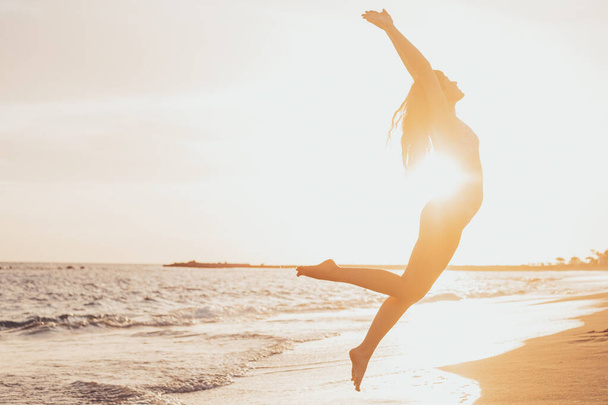 Одна щаслива і здорова молода жінка стрибає на піску пляжу розважається і насолоджується літом на відкритому повітрі. Красива приваблива дівчина грає
.  - Фото, зображення
