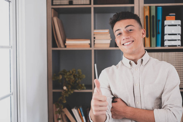Close up focus on male hand with thumbs up gesture. Smiling attractive young caucasian man employee recommending good service, satisfied with successful career in international company.  - 写真・画像