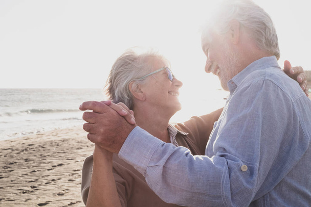 Пара з двох старих і зрілих щасливих літніх людей насолоджуються літніми танцями разом на пляжі на піску з заходом сонця на задньому плані. Відпочинок та дозвілля
   - Фото, зображення
