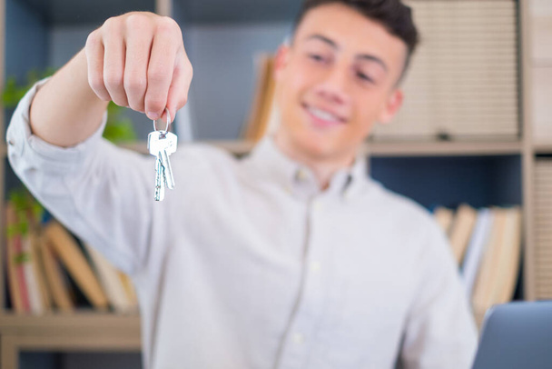 Focus on bunch of keys from house flat apartment in hand of smiling teenager. Blurred portrait of confident man professional realtor offering new dwelling real estate unit to potential buyer. Close up  - Photo, Image