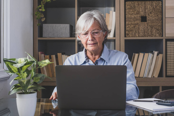 Onnellinen vanha valkoihoinen liikenainen hymyilee online-katselu webinar podcast kannettavan tietokoneen ja oppimisen kurssikonferenssin soittamalla tehdä muistiinpanoja istua työpöytä, verkko-oppimisen käsite  - Valokuva, kuva