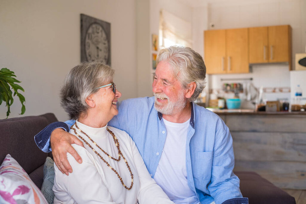 Portrait de couple de personnes âgées riant et s'amusant ensemble assis sur le canapé de la maison à l'intérieur. Deux personnes âgées et matures souriant et appréciant plaisanter.  - Photo, image