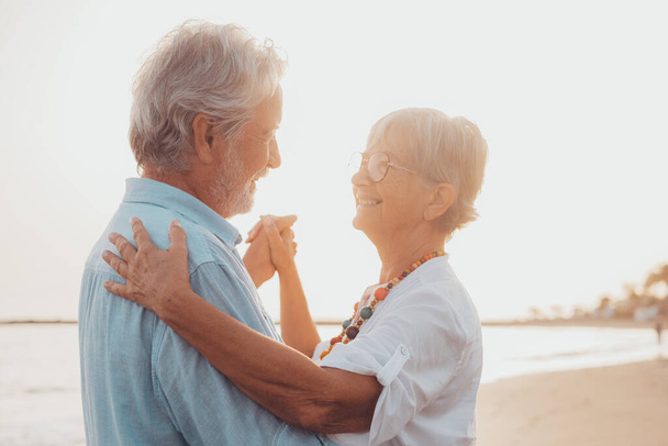 Couple de vieilles personnes mûres dansant ensemble et s'amusant sur le sable à la plage profiter et vivre l'instant. Portrait de personnes âgées amoureuses qui se regardent en s'amusant. - Photo, image