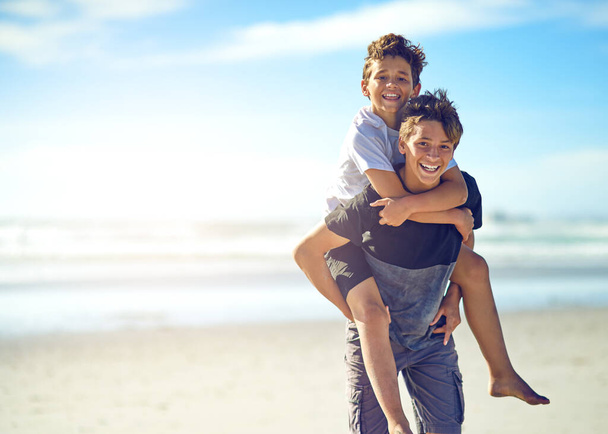 Мой брат и мой лучший друг. Портрет счастливого мальчика, катающего своего младшего брата на спине по пляжу - Фото, изображение
