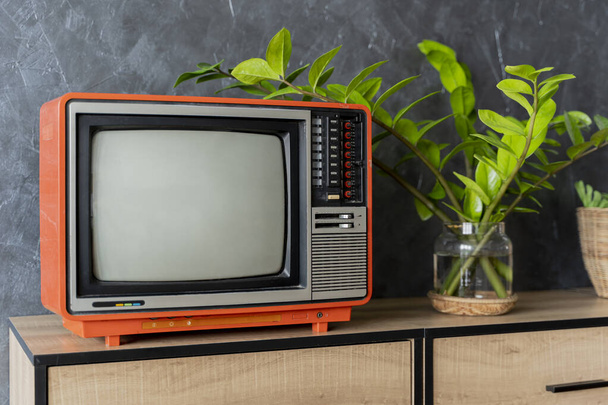 Old orange TV on a wooden cabinet in the room of the house. Loft wall. Warm atmosphere. vintage set of tv equipments concept. - 写真・画像