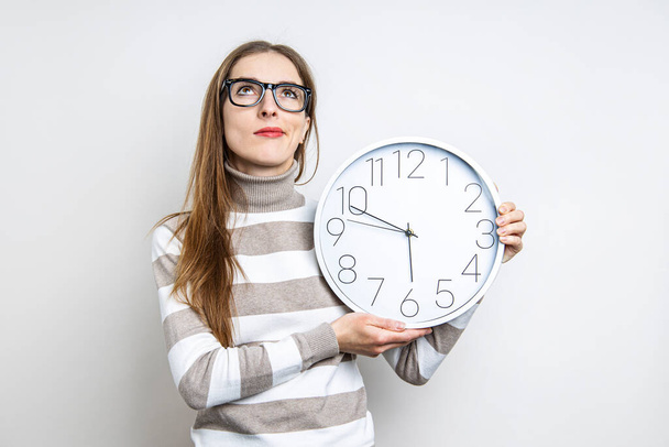 Young woman pensive looking up holding a clock on a light background  - Photo, Image