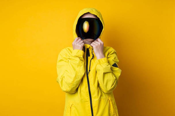Young woman in a mask of cyberpunk goggles in a yellow jacket on a yellow background. - Foto, Bild