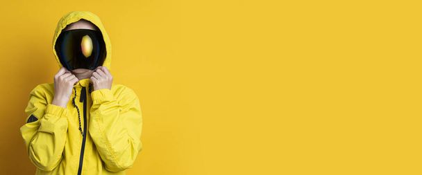 Young woman in a mask of cyberpunk goggles in a yellow jacket on a yellow background. Banner. - Photo, Image