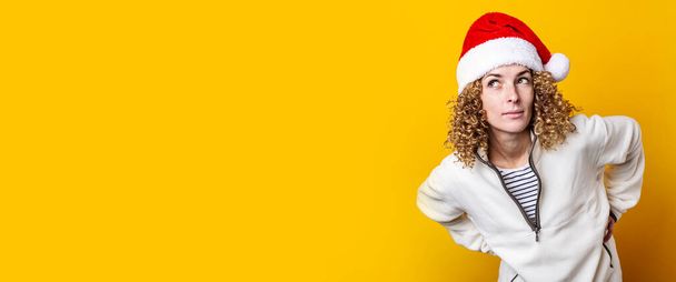 Smiling curly young woman in a santa hat on a yellow background. Banner  - Foto, Imagem
