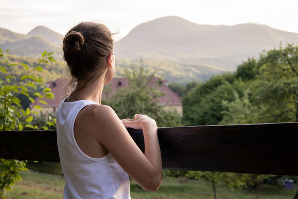 Молодая женщина в белой майке наслаждается красивым природным ландшафтом с видом на горы. - Фото, изображение