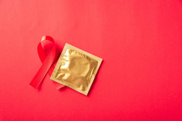 Red bow ribbon symbol HIV, AIDS cancer awareness and condom with shadows, studio shot isolated on red background, Healthcare medicine sexually concept, World AIDS Day - Фото, изображение