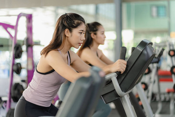 Zwei asiatische Frauen trainieren im Fitnessstudio, indem sie Seile ziehen Asiatische Frau in Sportbekleidung läuft auf einem Laufband Laufgerät Bleiben Sie konzentriert, konzentrieren Sie sich auf das Training, gesund und fit. - Foto, Bild