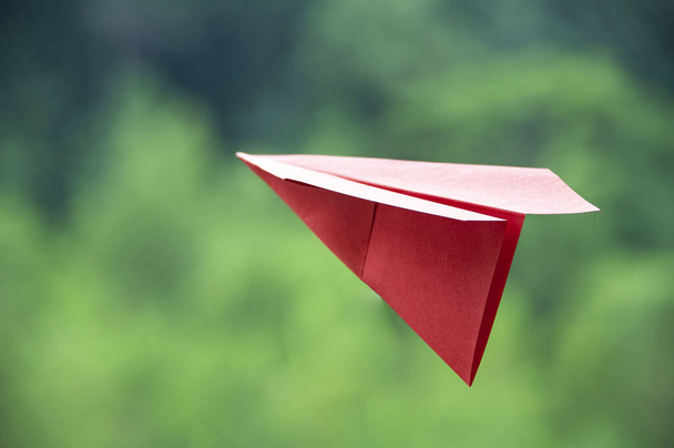 Flying red paper plane with blurred green nature background. - Photo, Image