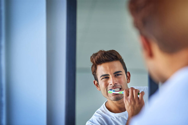 Making oral health a priority. Portrait of a happy young man brushing his teeth at home - Photo, Image